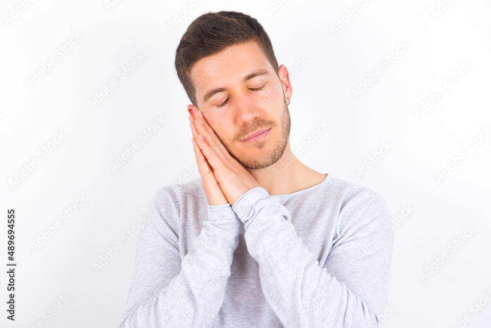 young caucasian man wearing grey sweater over white background leans on pressed palms closes eyes and has pleasant smile dreams about something young caucasian man wearing grey sweater over white background leans on pressed palms closes eyes and has pleasant smile dreams about something