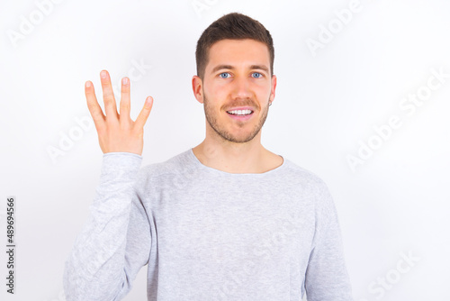 young caucasian man wearing grey sweater over white background smiling and looking friendly, showing number four or fourth with hand forward, counting down © Roquillo