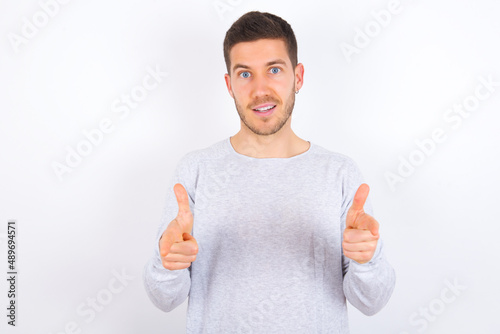 young caucasian man wearing grey sweater over white background directs fingers at camera selects someone. I recommend you. Best choice