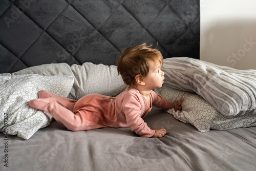 Small caucasian baby lying down on the belly on the bed with wet urine stain on the sheet and clothes looking to the side Bedwetting child pee on the bed photo