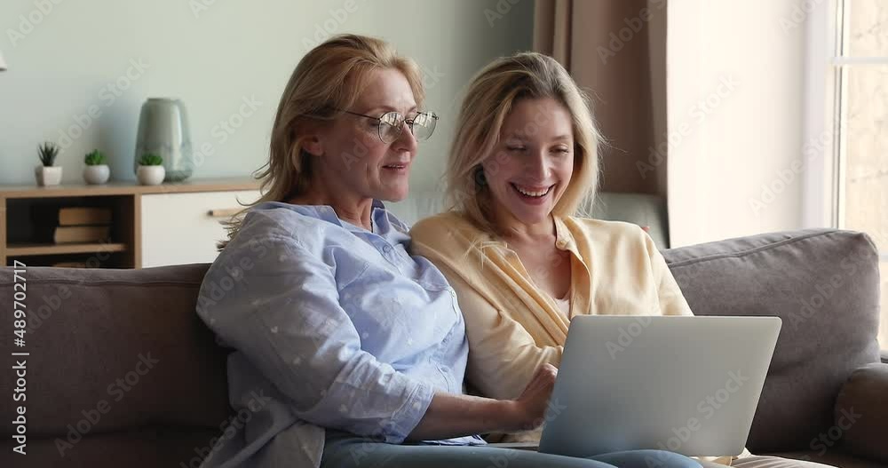 Attractive middle-aged 60s woman her young adult millennial daughter discuss online purchase sit on cozy sofa with laptop, enjoy time together, buy on internet. Modern tech, connection, fun concept Attractive middle-aged 60s woman her young adult millennial daughter discuss online purchase sit on cozy sofa with laptop, enjoy time together, buy on internet. Modern tech, connection, fun concept