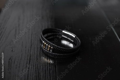Black leather male bracelet with metal pendant on the dark wooden desk
