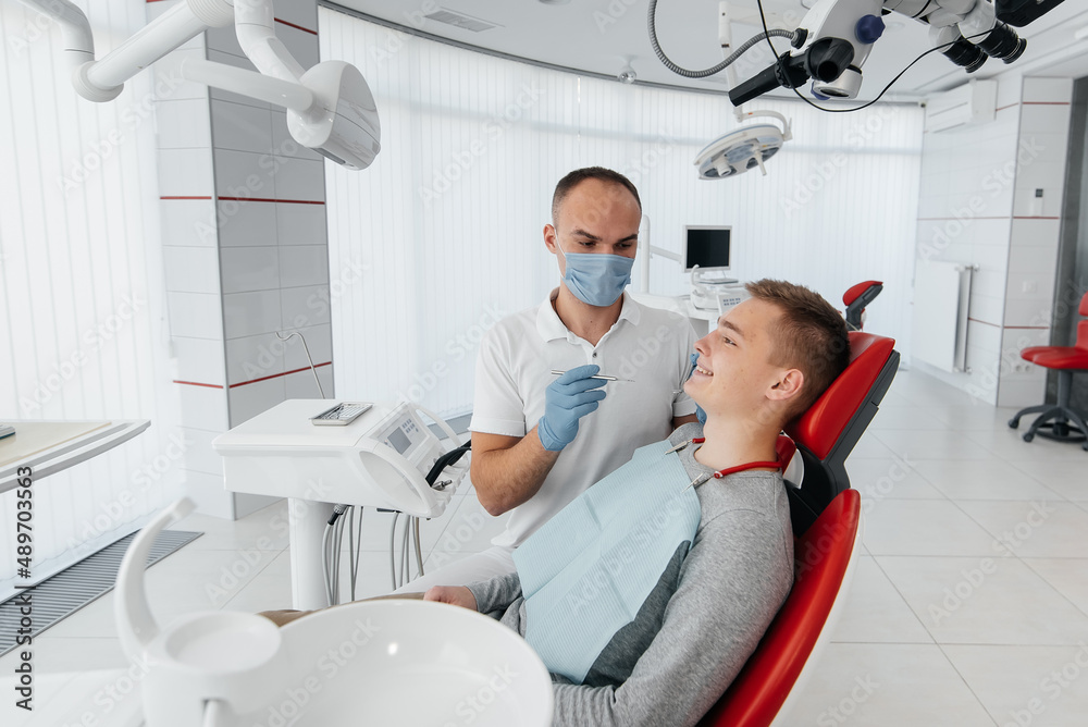 Obraz premium A young dentist examines and treats the teeth of a young man in modern white dentistry close-up. Dental prosthetics, treatment and teeth whitening. Modern dentistry. Prevention.