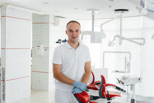 Wallpaper Mural A young dentist stands near a red dental chair and smiles in modern white dentistry. Treatment and prevention of caries from youth. Modern dentistry and prosthetics. Torontodigital.ca