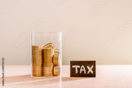 Many gold coins were put in a glass jar and wooden signs with tax messages. Annual income tax return to the government sector concept.