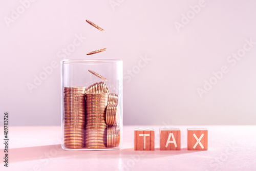 Many gold coins were put in a glass jar and wooden signs with tax messages. Annual income tax return to the government sector concept.