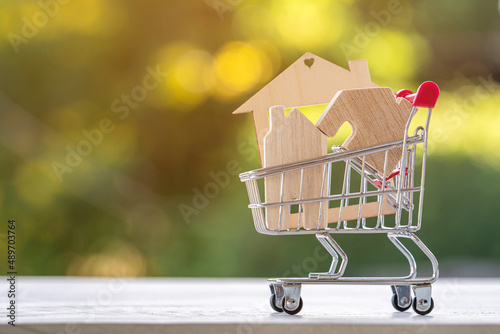 Model of a house in a shopping cart placed on a wooden table in the garden. Financial planning or principles for buying a house and real estate loan concept.