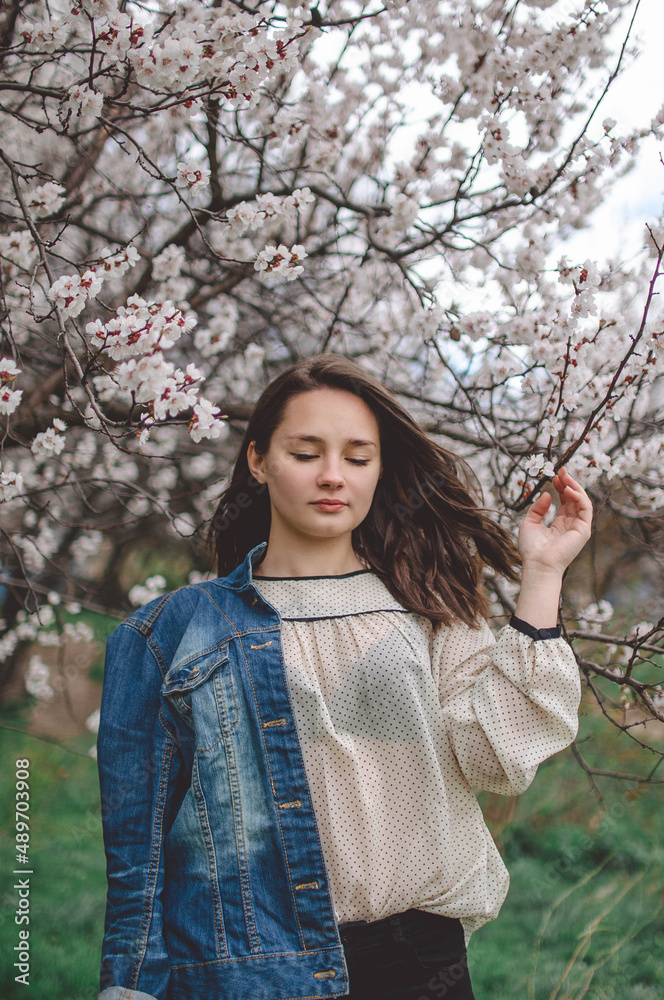 beautiful girl model in a denim jacket in spring garden in flowers