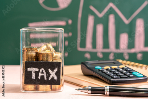 Many gold coins were put in a glass jar and wooden signs with tax messages, Next comes a calculator and an account book. Annual income tax return to the government sector concept.
