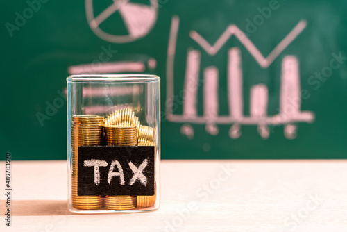 Many gold coins were put in a glass jar and wooden signs with tax messages. Annual income tax return to the government sector concept.