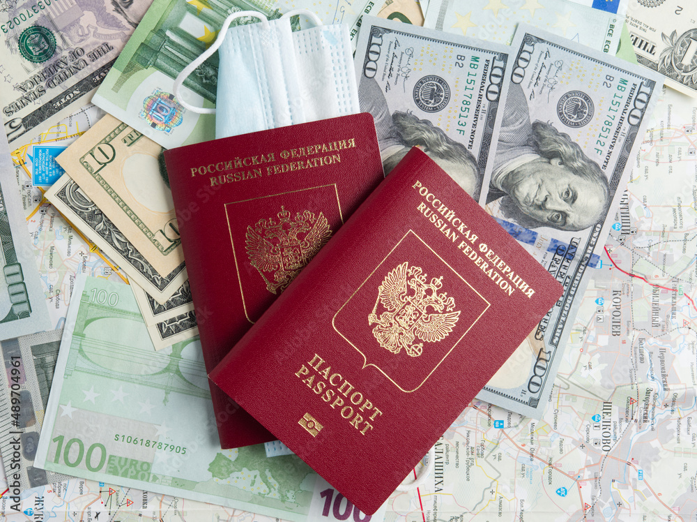 Two Russian passports are on dollar and euro bills. A medical mask is attached to one of the passports. The concept of traveling during a pandemic and diseases. Top view, flat lay Two Russian passports are on dollar and euro bills. A medical mask is attached to one of the passports. The concept of traveling during a pandemic and diseases. Top view, flat lay