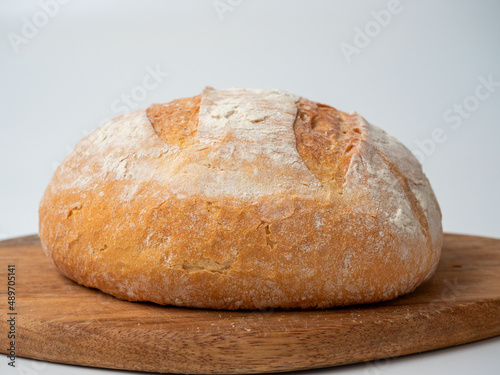 A close-up of freshly baked wheat bread with a crispy crust lies on a wooden tray. Side view, bakery concept