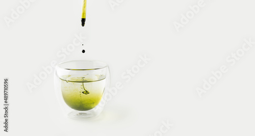 Liquid chlorophyll extract is pipetted into a glass of water. White background. The concept of superfoods, healthy eating, detox and wellness. Banner, place for text