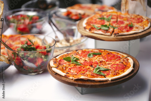 There are many different freshly prepared pizzas on the buffet table.