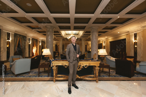 Businessman man in a classic stands in the luxurious interior of the hotel and shows a thumbs up.