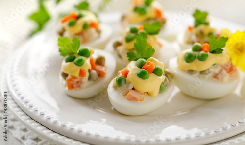 Hard- boiled eggs divided into halves and stuffed with traditional  vegetable salad with mayonnaise served on a white plate close up view. Easter food photo