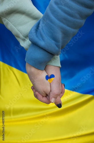 male and female hands together, on them a heart painted in yellow and blue colors of the Ukrainian flag. Family, unity, support. Russia's invasion of Ukraine, a request for help to the world community photo
