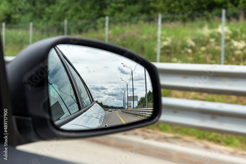 Close-up of a car's rear-view mirror, which reflects the road and other cars. Selective focus.