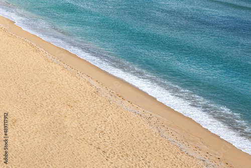 View from above. Turquoise sea water and yellow sand of the beach strip divide the frame diagonally.