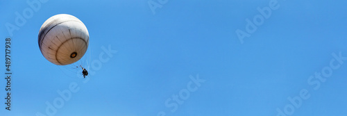 Rise into the sky in a hot air balloon above the city. White hot air balloon against the blue sky. Banner format.