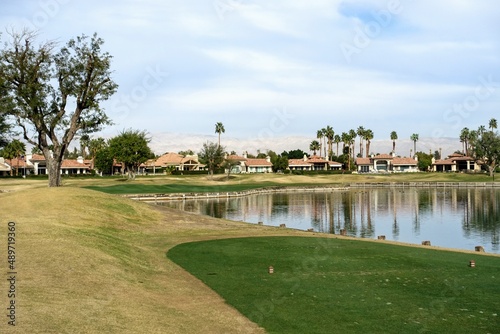 A beautiful photo of a par 3 over a lake, from the perspective of the tee box looking towards the green.  The fairway is very undulated.  In Palm Springs, California, United States