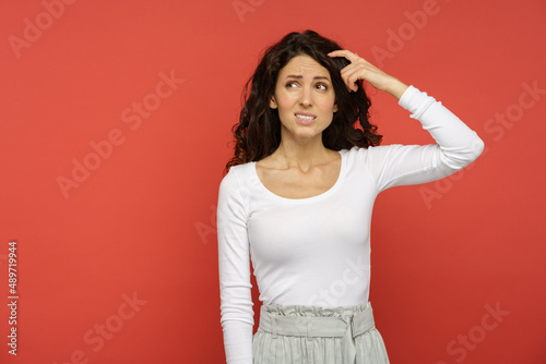 Closeup shot of curly millennial female minded thinking, creating solution planning idea looking up with hand on head and hair. Young woman pensive thinking isolated on red wall on copy space