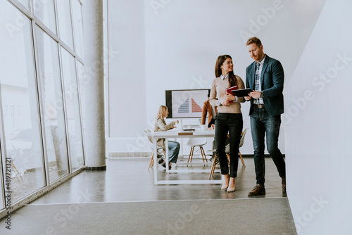 Young entrepreneur couple walking together and using digital tablet in the modern office