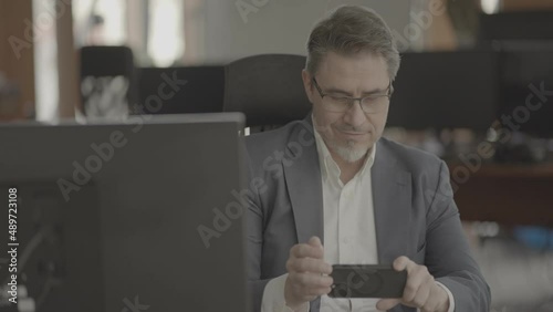 Business portrait - confident businessman sitting at desk working in office, using phone. Happy mid adult man in shirt and jacket, smiling. Video in LOG format - S-LOG3 Cine. photo