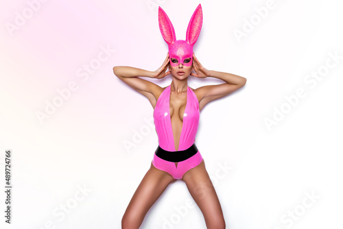 Fototapet Sexy blonde woman posing in latex pink costume and pink bunny mask on white background