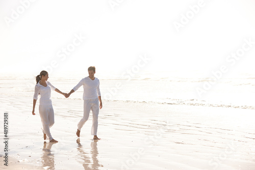 Holding hands through natures beauty. Full length shot of an attractive young couple dressed in white walking along a beach.