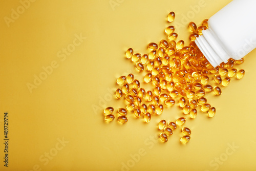 Golden Omega-3 fish oil capsules poured out of a jar on a yellow background photo