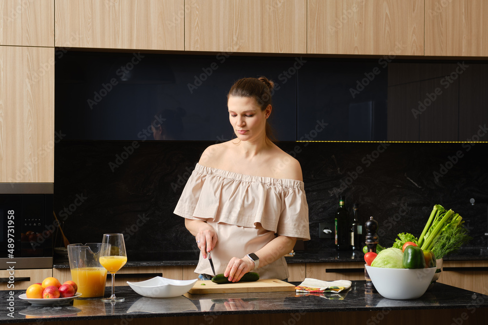 Pregnant woman in the kitchen cutting cucumber