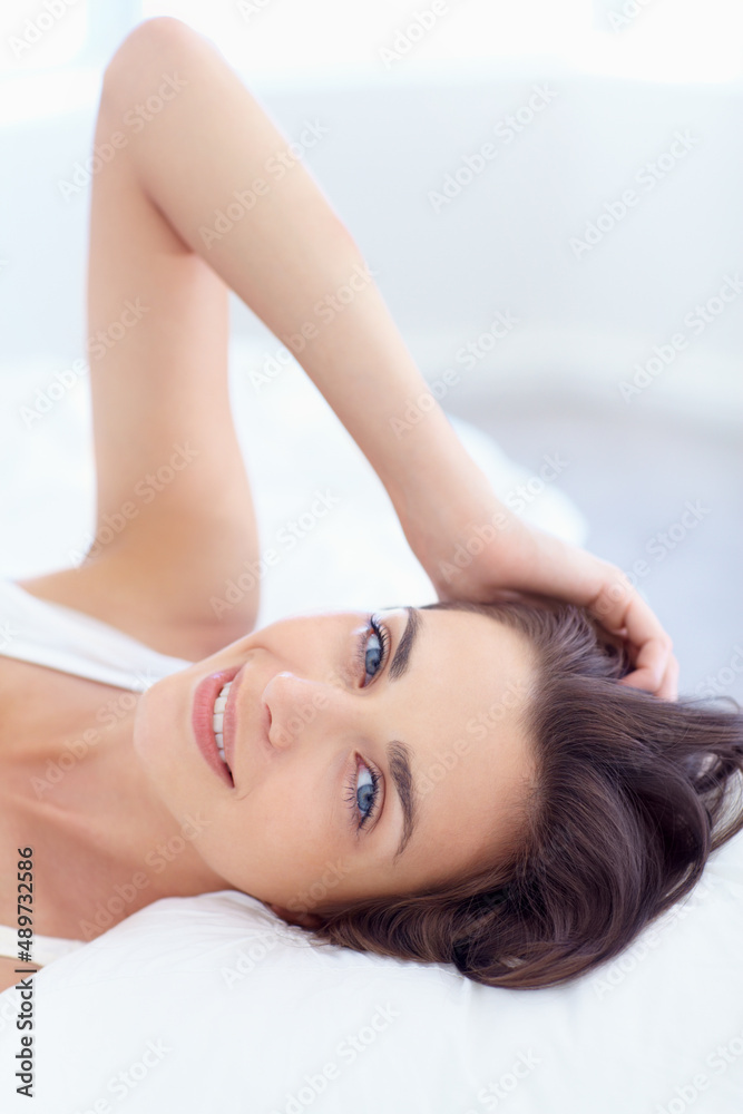 Young and beautiful. Portrait of a pretty young woman smiling at the camera while lying in bed.