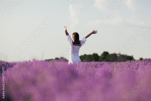 Obraz na płótnie Beautiful young woman with a white dress standing in the middle of a lavender field with hands up. w salonie