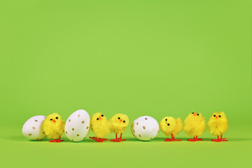 Small decorative easter chickens and eggs in a row on green background