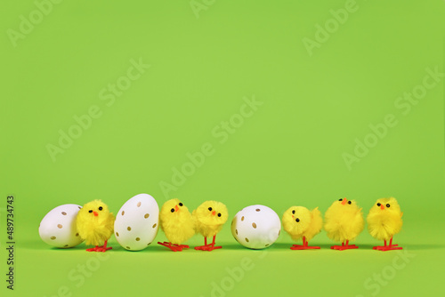 Small decorative easter chickens and eggs in a row on green background
