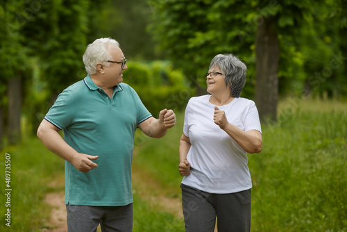 Portrait of a happy senior couple on their morning run in a green park or forest in the countryside. Energetic old man and woman in their 60s enjoying active exercise and running workout in nature