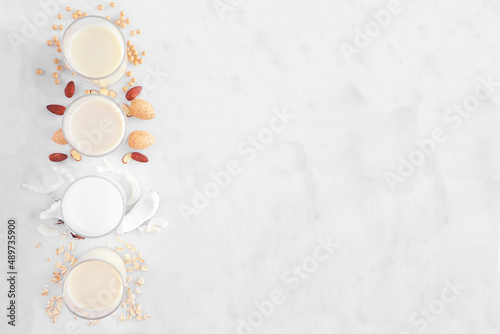 Vegan  plant based  non dairy milk background. Assortment in drinking glasses with ingredients. Above view side border over a white marble background. Copy space.