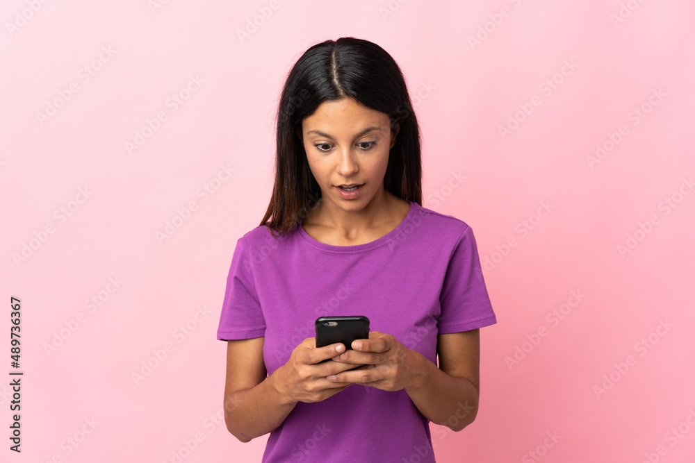 Caucasian girl isolated on pink background looking at the camera while using the mobile with surprised expression Caucasian girl isolated on pink background looking at the camera while using the mobile with surprised expression