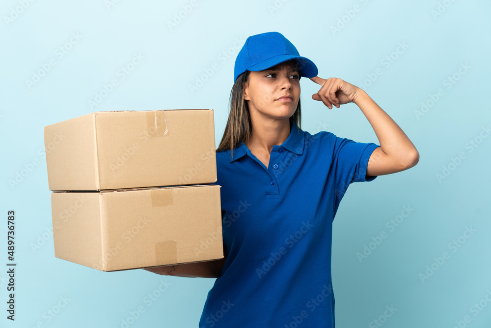 Young delivery woman isolated on blue background having doubts and thinking