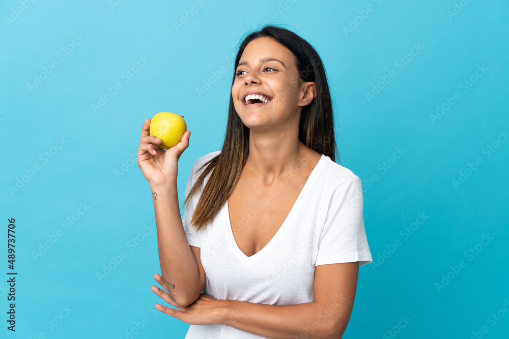 Caucasian girl isolated on blue background with an apple and happy
