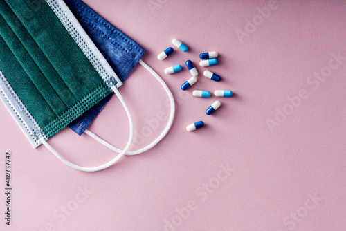 Several pills and oral capsules on a disposable medical face mask against pink background.