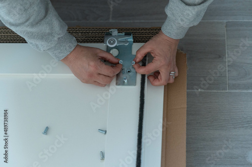 Hands hold screws to attach iron fittings to white wooden boards on the floor, on top of cardboard.
