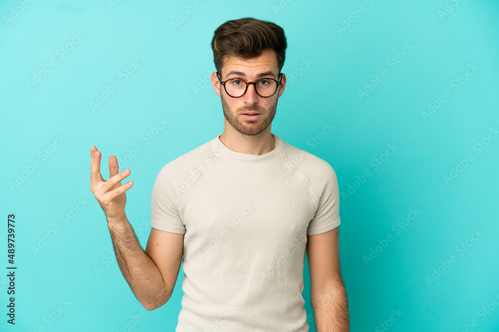 Fototapeta premium Young caucasian handsome man isolated on blue background making doubts gesture