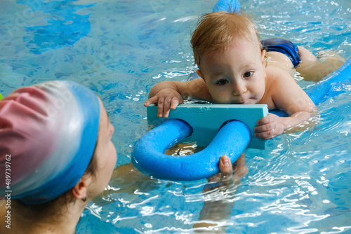 Early swimming coach training to swim baby boy in indoor pool. Playing activity for infant with mother, child physical development in water with joy and fun. Accessories and toys for diving lesson photo