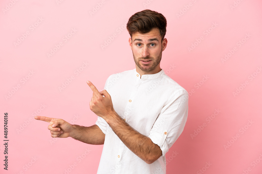 Young caucasian handsome man isolated on pink background frightened and pointing to the side