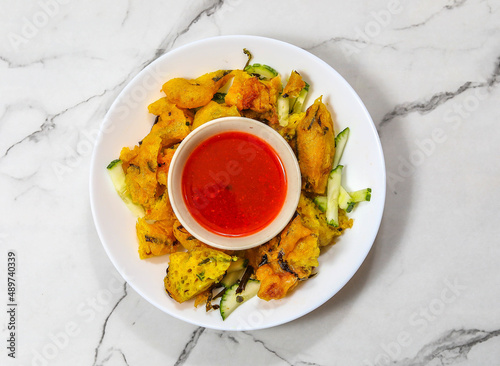 deep-fried cucur udang prawn fritters with chili sauce served in white dish isolated on marble background top view