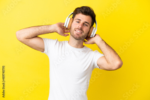 Young caucasian handsome man isolated on yellow background listening music