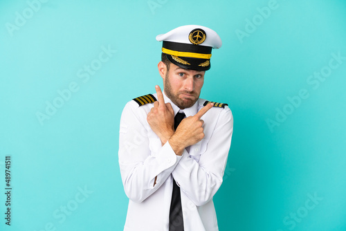 Airplane caucasian pilot isolated on blue background pointing to the laterals having doubts