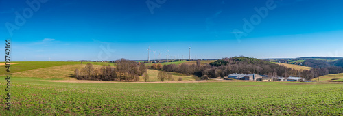 Panoramic view over beautiful farm landscape with early spring agriculture field, wind turbines to produce green energy near Mittweida, Germany, at blue sunny sky.